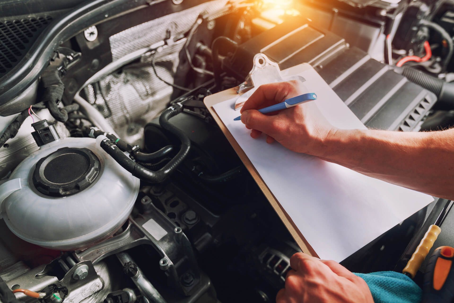 Ein Mechaniker inspiziert einen Motor, während er sich Notizen auf einem Klemmbrett macht, umgeben von verschiedenen Autoteilen und Werkzeugen.